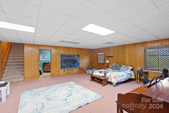 carpeted bedroom with wooden walls and a paneled ceiling