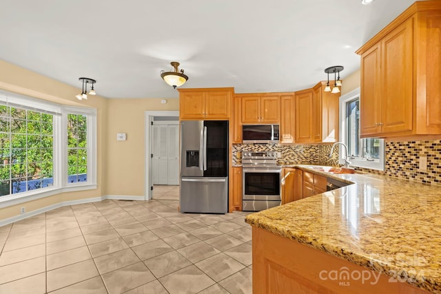 kitchen featuring tasteful backsplash, light stone countertops, stainless steel appliances, sink, and decorative light fixtures