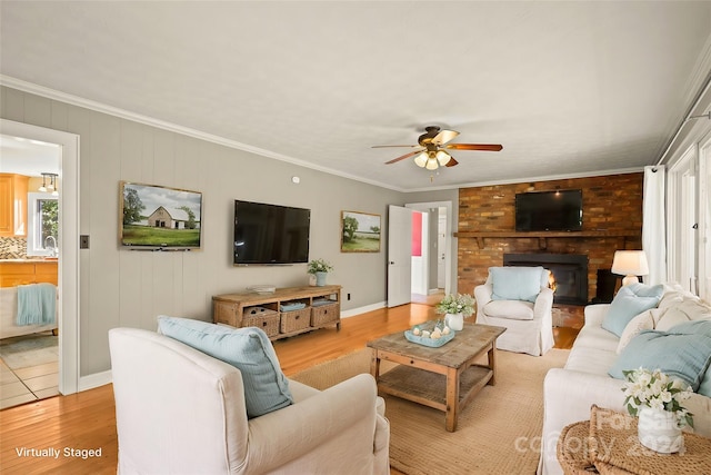 living room with light hardwood / wood-style flooring, ornamental molding, sink, a brick fireplace, and ceiling fan