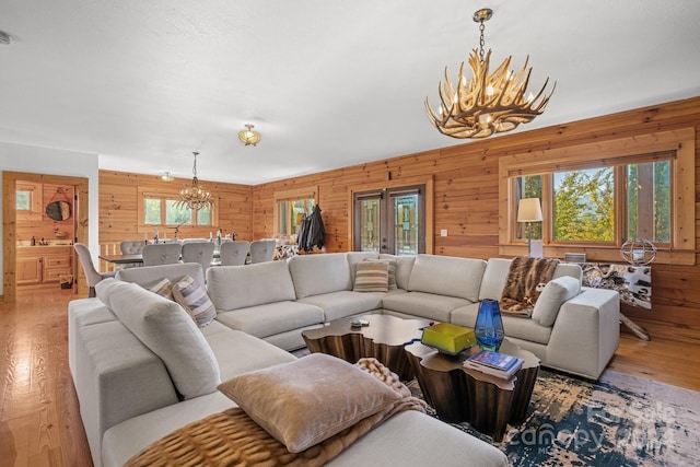 living room with light hardwood / wood-style floors, wood walls, and an inviting chandelier