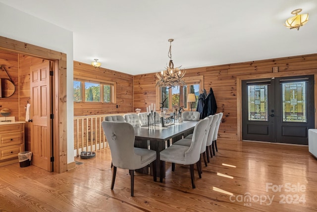 dining room featuring french doors, a notable chandelier, hardwood / wood-style flooring, and wooden walls