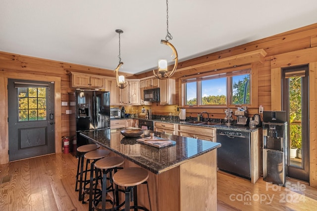 kitchen with hanging light fixtures, light hardwood / wood-style flooring, black appliances, sink, and a center island