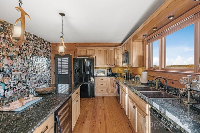 kitchen featuring light hardwood / wood-style flooring, hanging light fixtures, dark stone countertops, sink, and black appliances