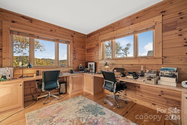 office with light hardwood / wood-style floors, a healthy amount of sunlight, built in desk, and wooden walls