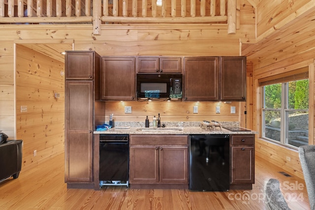 kitchen with light hardwood / wood-style floors, black appliances, sink, and wooden walls