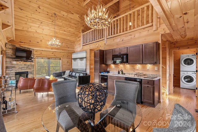 dining area with wood walls, stacked washer / dryer, a stone fireplace, light hardwood / wood-style floors, and high vaulted ceiling