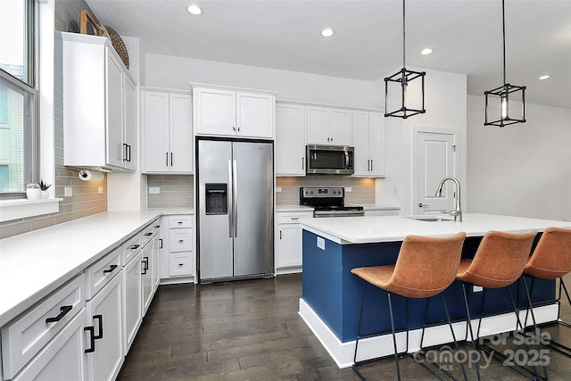 kitchen featuring sink, stainless steel appliances, an island with sink, pendant lighting, and white cabinets