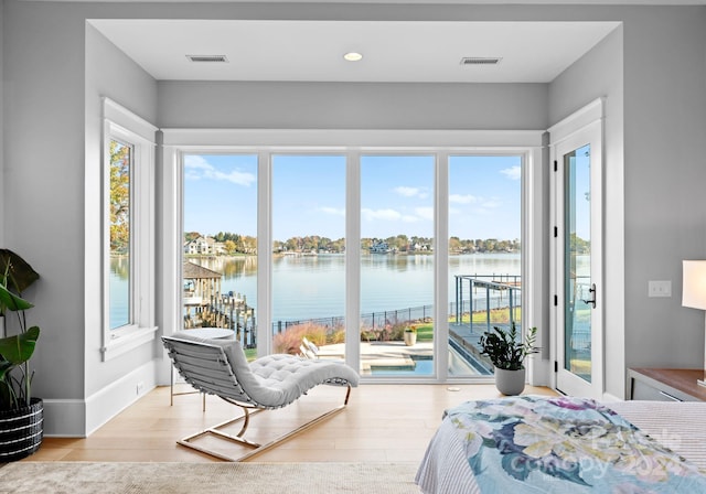 bedroom with access to outside, multiple windows, light hardwood / wood-style flooring, and a water view