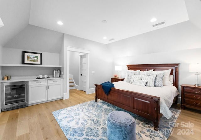 bedroom featuring bar area, beverage cooler, lofted ceiling, and light wood-type flooring