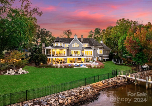 back house at dusk with a yard, a patio area, a balcony, and a fire pit