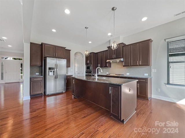 kitchen with tasteful backsplash, stainless steel appliances, pendant lighting, dark wood-type flooring, and a center island with sink