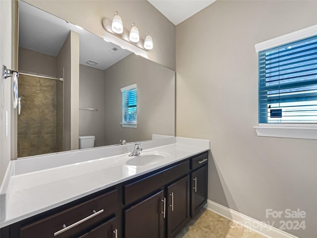 bathroom featuring vanity, a tile shower, toilet, and tile patterned floors