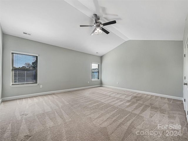 empty room featuring ceiling fan, vaulted ceiling, a wealth of natural light, and light colored carpet