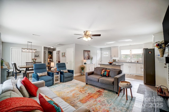 living room with light wood-style flooring, baseboards, and ceiling fan with notable chandelier