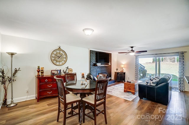 dining area with light wood-style floors, a brick fireplace, baseboards, and ceiling fan