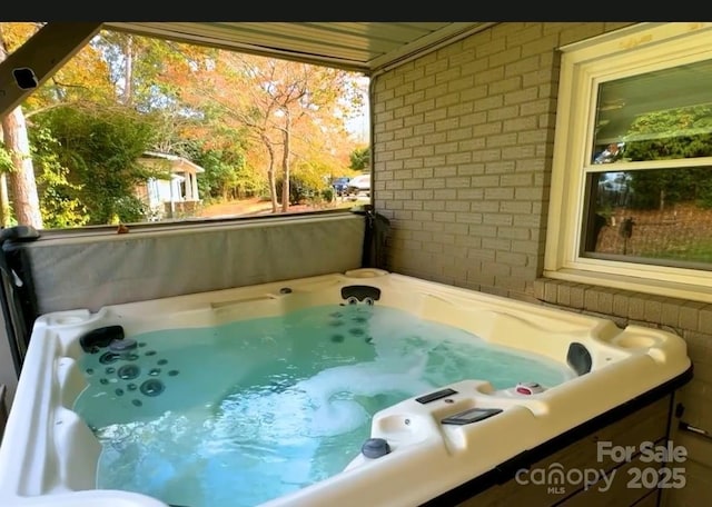 exterior space featuring a jacuzzi, brick wall, and a healthy amount of sunlight