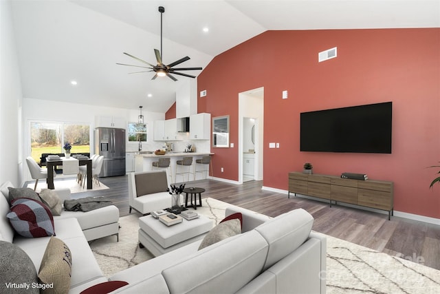 living room with ceiling fan, high vaulted ceiling, sink, and light hardwood / wood-style floors