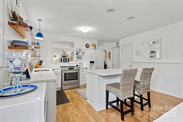 kitchen featuring a kitchen bar, stainless steel electric range oven, white refrigerator with ice dispenser, white cabinetry, and hanging light fixtures