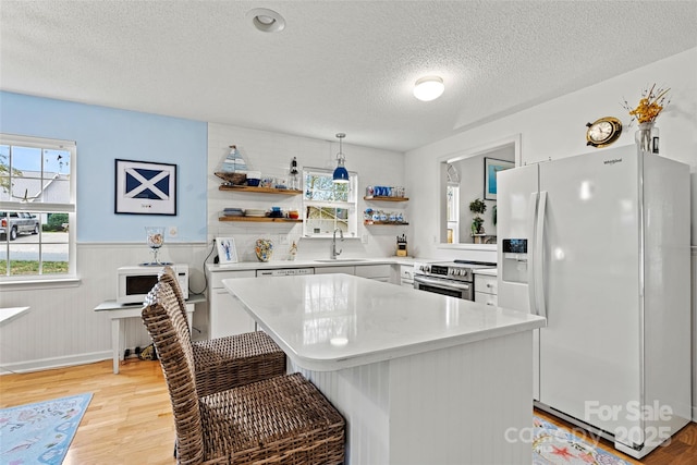 kitchen with a kitchen island, white appliances, a textured ceiling, and a wealth of natural light