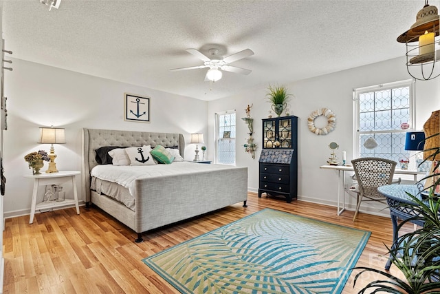 bedroom with multiple windows, ceiling fan, wood-type flooring, and a textured ceiling