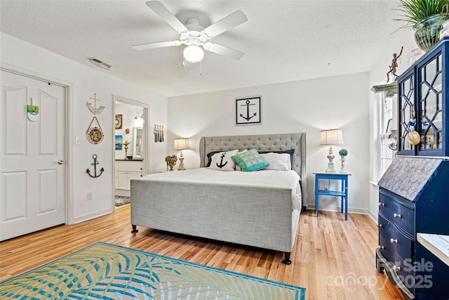 bedroom featuring ceiling fan, light hardwood / wood-style floors, a textured ceiling, and ensuite bath