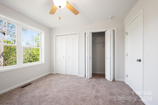 unfurnished bedroom featuring ceiling fan, light colored carpet, and two closets