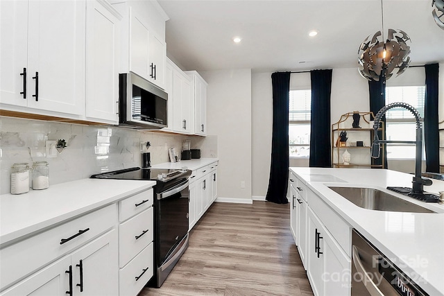 kitchen with light hardwood / wood-style floors, white cabinetry, sink, appliances with stainless steel finishes, and decorative light fixtures