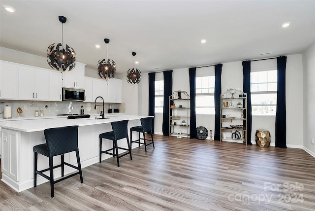 kitchen featuring white cabinetry, a breakfast bar area, hanging light fixtures, a spacious island, and light hardwood / wood-style flooring