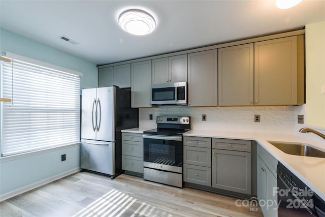 kitchen with decorative backsplash, sink, gray cabinetry, light hardwood / wood-style floors, and stainless steel appliances