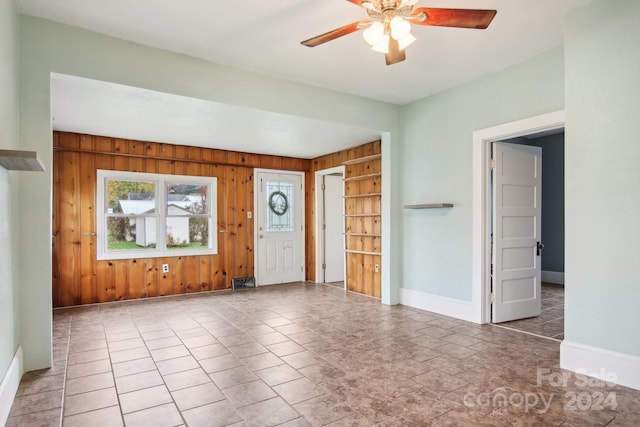 foyer entrance featuring tile patterned flooring, ceiling fan, and wooden walls