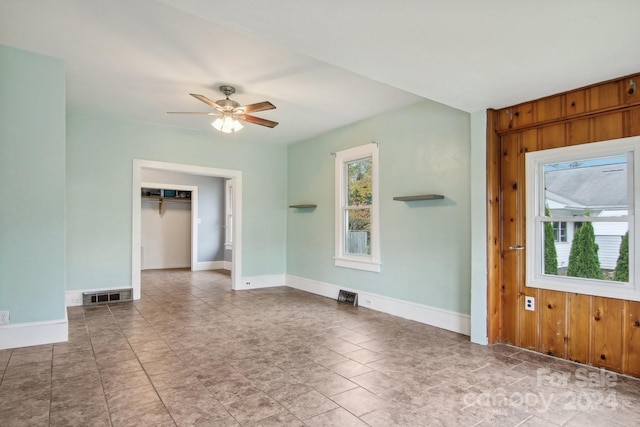 unfurnished room with ceiling fan and wood walls