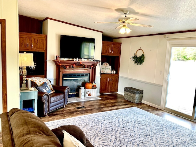 living room with a tile fireplace, ornamental molding, dark hardwood / wood-style flooring, a textured ceiling, and ceiling fan