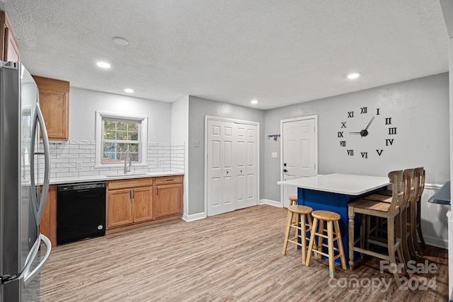 kitchen with a kitchen breakfast bar, stainless steel refrigerator, dishwasher, light hardwood / wood-style floors, and sink