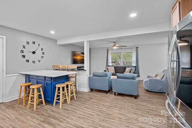 living room featuring light hardwood / wood-style floors, a textured ceiling, bar area, and ceiling fan