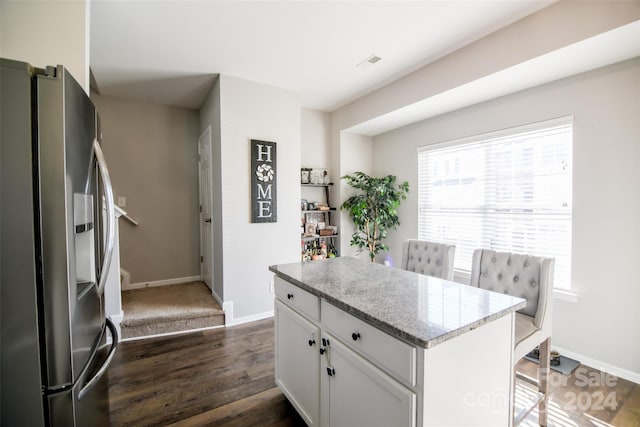 kitchen featuring white cabinets, dark hardwood / wood-style floors, stainless steel fridge, light stone countertops, and a kitchen bar