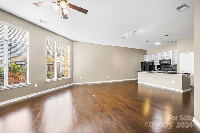 unfurnished living room featuring rail lighting, dark wood-type flooring, and ceiling fan