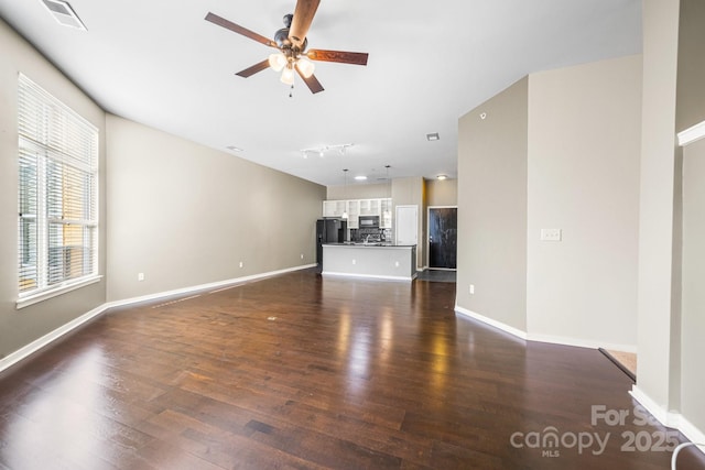 unfurnished living room with baseboards, dark wood-style floors, visible vents, and ceiling fan