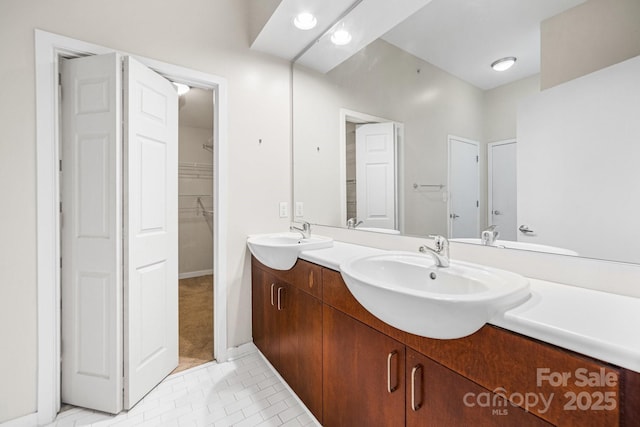 bathroom featuring double vanity, a walk in closet, a sink, and tile patterned flooring