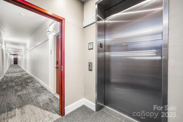 hallway featuring elevator, carpet flooring, and baseboards