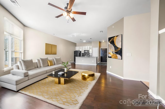 living room with baseboards, ceiling fan, visible vents, and dark wood finished floors