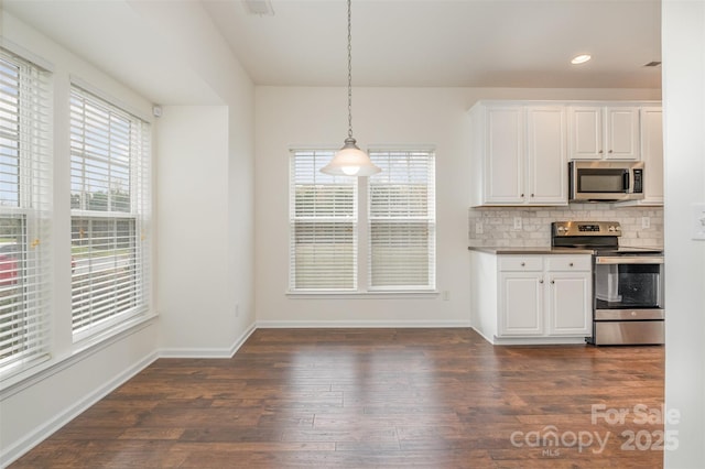 kitchen with dark wood-type flooring, appliances with stainless steel finishes, white cabinetry, backsplash, and decorative light fixtures