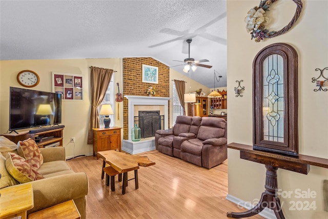 living room with a fireplace, light hardwood / wood-style floors, vaulted ceiling, and ceiling fan