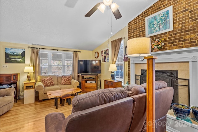 living room featuring brick wall, vaulted ceiling, ceiling fan, light hardwood / wood-style flooring, and a fireplace