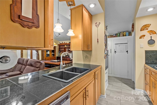 kitchen featuring pendant lighting, a textured ceiling, stainless steel dishwasher, and sink