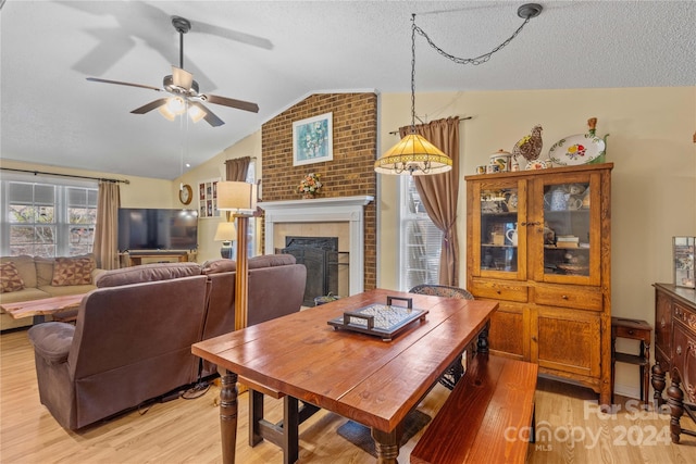 dining space with a brick fireplace, a textured ceiling, ceiling fan, light hardwood / wood-style floors, and lofted ceiling