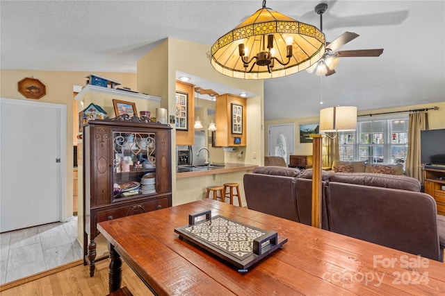 dining space featuring ceiling fan with notable chandelier, sink, vaulted ceiling, light wood-type flooring, and a textured ceiling