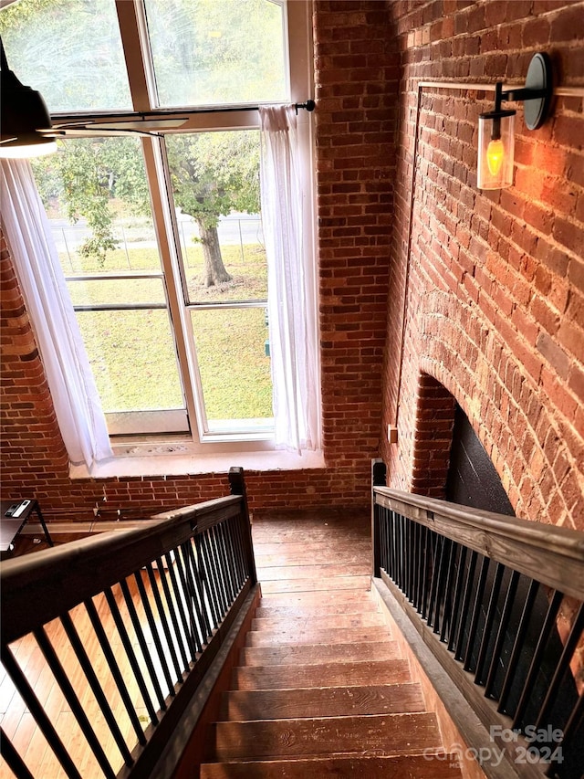 stairs featuring hardwood / wood-style floors, brick wall, and a wealth of natural light