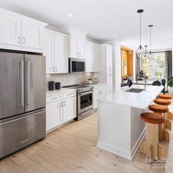 kitchen with a center island with sink, hanging light fixtures, white cabinetry, light wood-type flooring, and stainless steel appliances