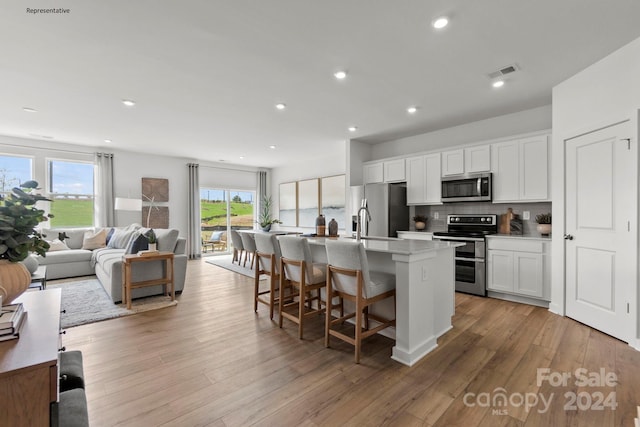 kitchen with a kitchen island with sink, stainless steel appliances, white cabinets, and light hardwood / wood-style flooring