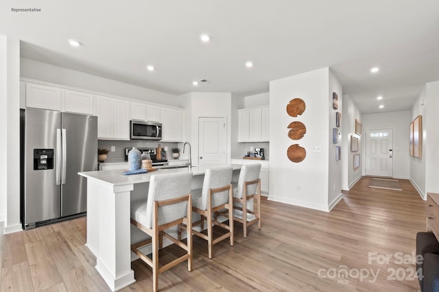 kitchen with a kitchen island with sink, light wood-type flooring, stainless steel appliances, and white cabinets